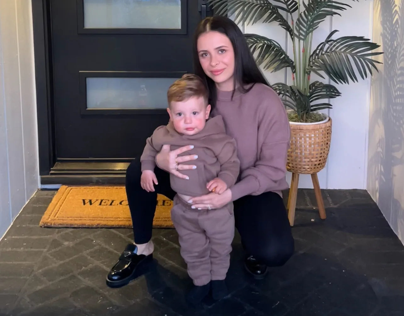 Woman holding child by door with welcome mat | Sleepy Baby