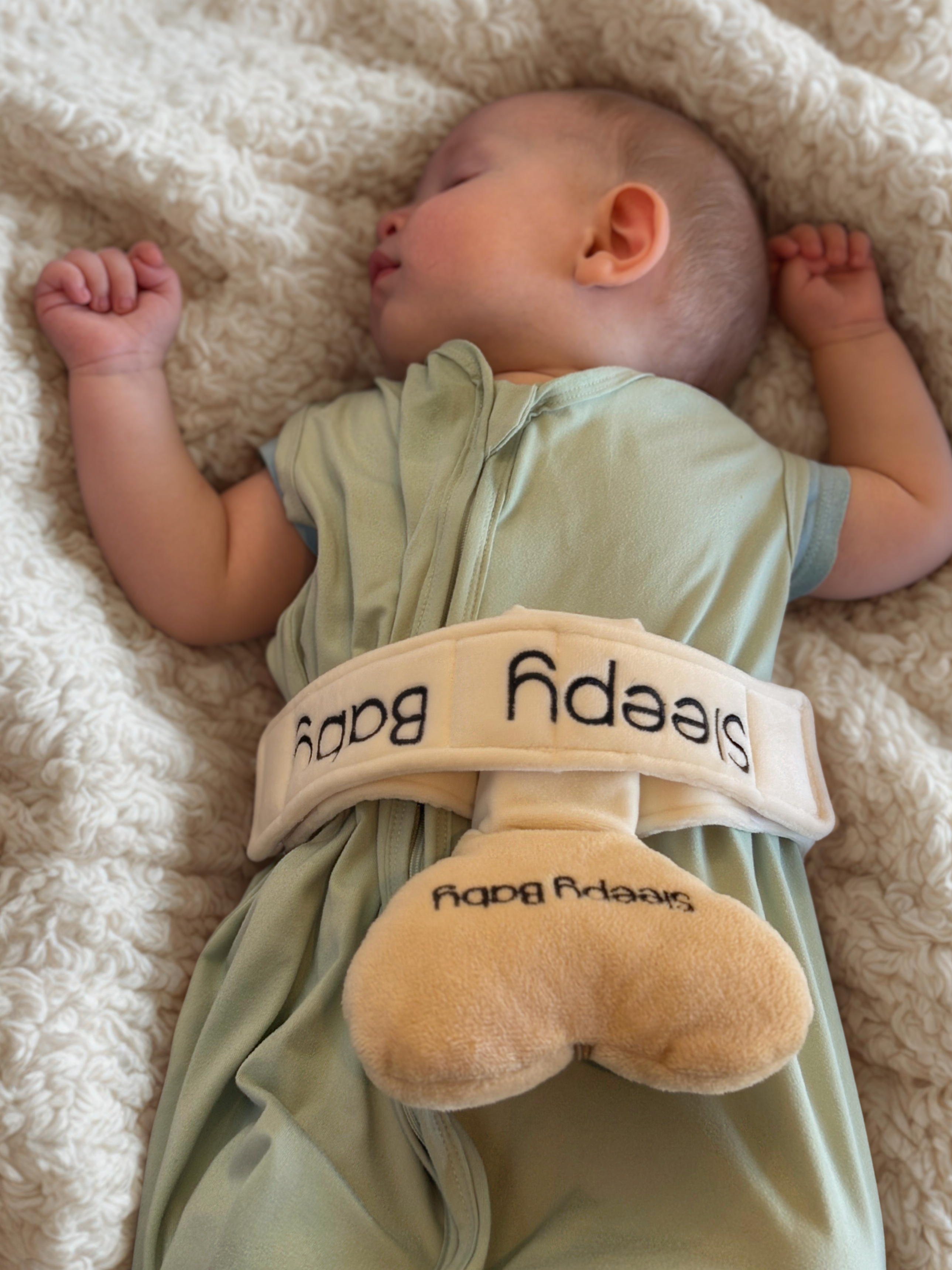 Baby wearing a green onesie with  Sleepy Baby Sleep Aid device on a soft surface.